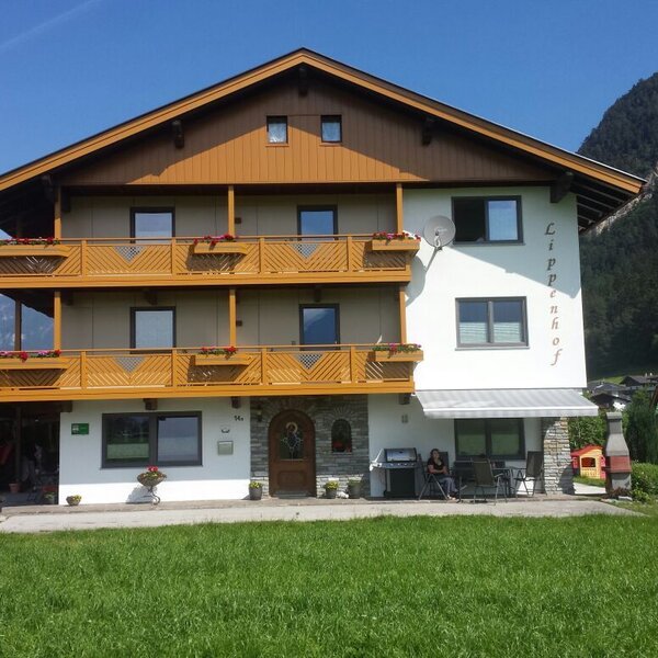Außenansicht des Bauernhofs mit Holzbalkonen und einem Kinderspielplatz im Gartenbereich.