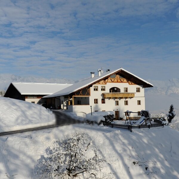 Der Bauernhof in verschneiter Winterlandschaft mit Zufahrtsweg und Blick auf die Berge.