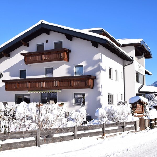 The snow-covered exterior of the Farm House, featuring multiple wooden balconies and visible mountains in the winter landscape.