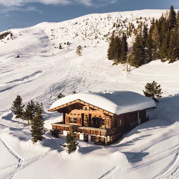 Die Holz-Alm, schneebedeckt und umgeben von Skipisten mit sichtbaren Skispuren und Nadelbäumen.
