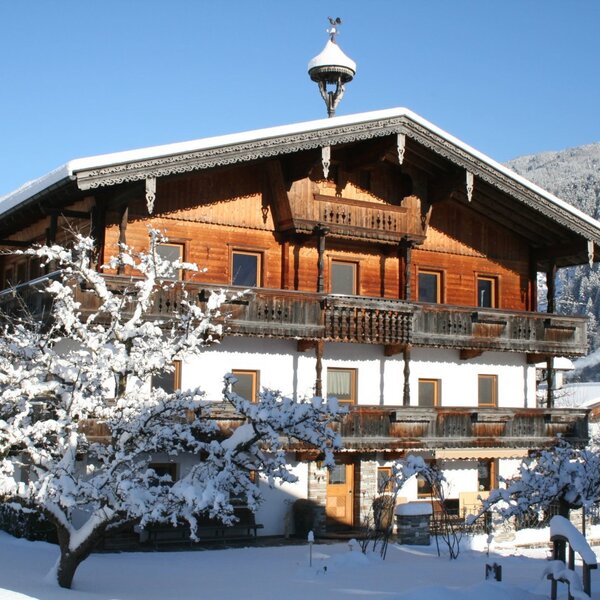 The snow-covered Farm House exterior, showcasing its traditional wooden design and balconies, set against a mountainous backdrop.
