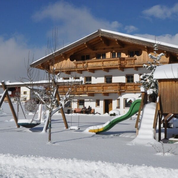 The snow-covered exterior of the Farm House, featuring a children's playground with swings and a slide, and a church steeple in the background.