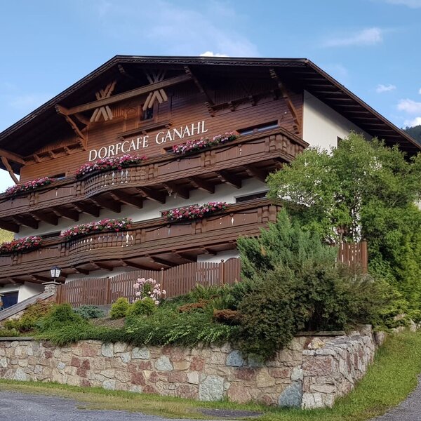 Die Außenansicht des Bauernhofs mit traditionellen Holzbalkonen, die mit Blumen geschmückt sind, und einer Steinmauer.