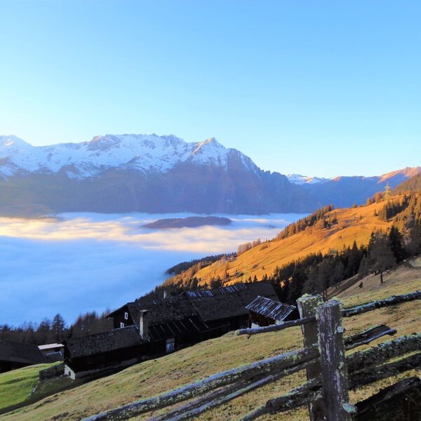 View of the snow-capped mountains and a cloud-filled valley from the Alpine Hut's hillside setting.