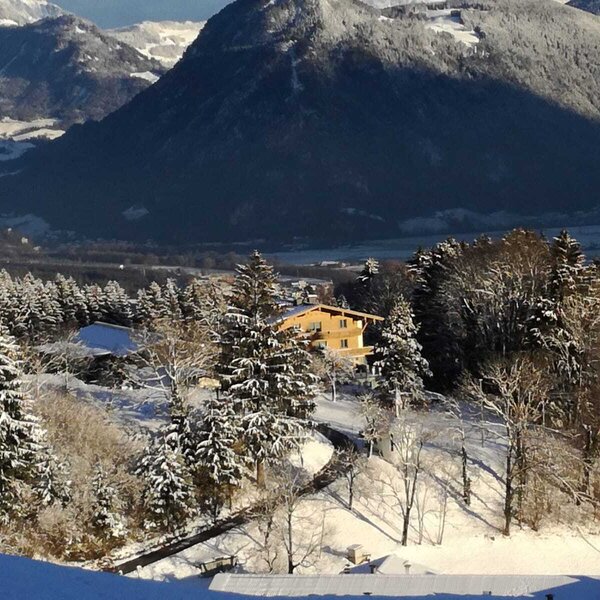 Außenansicht des Bauernhofs im Winter mit verschneiten Bäumen und Bergen im Hintergrund.