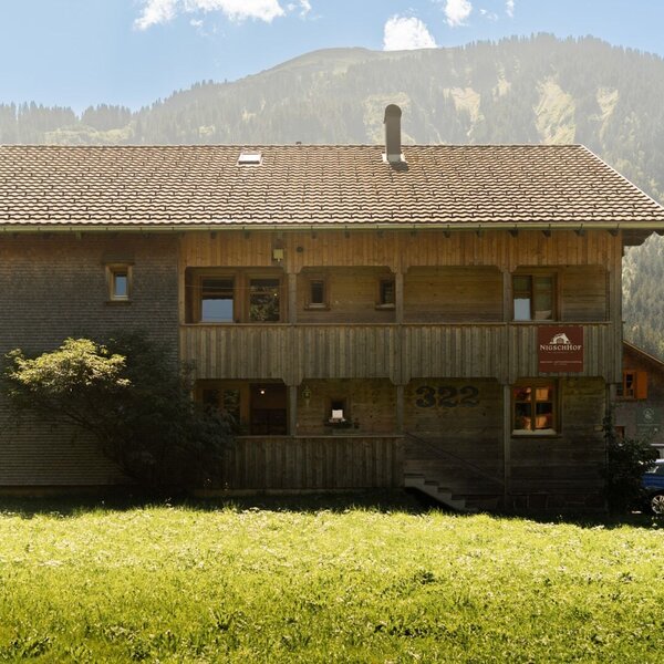 Exterior view of the Farm House, featuring a wooden facade, a multi-level design with a balcony, and available parking, set against a mountain and forest backdrop.